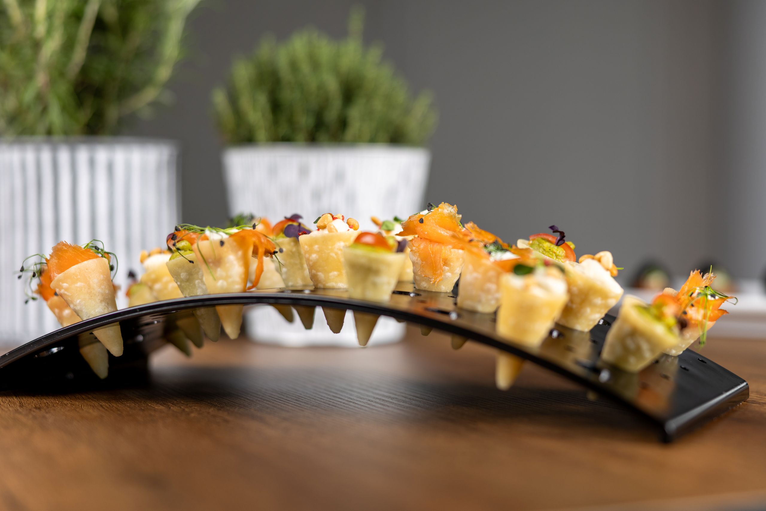 Mit Lachs und Salat gefüllte kleine Hörnchen in einem brückenartigem Ständer auf einem Tisch; im Hintergrund stehen zwei Kräuter in Töpfen.