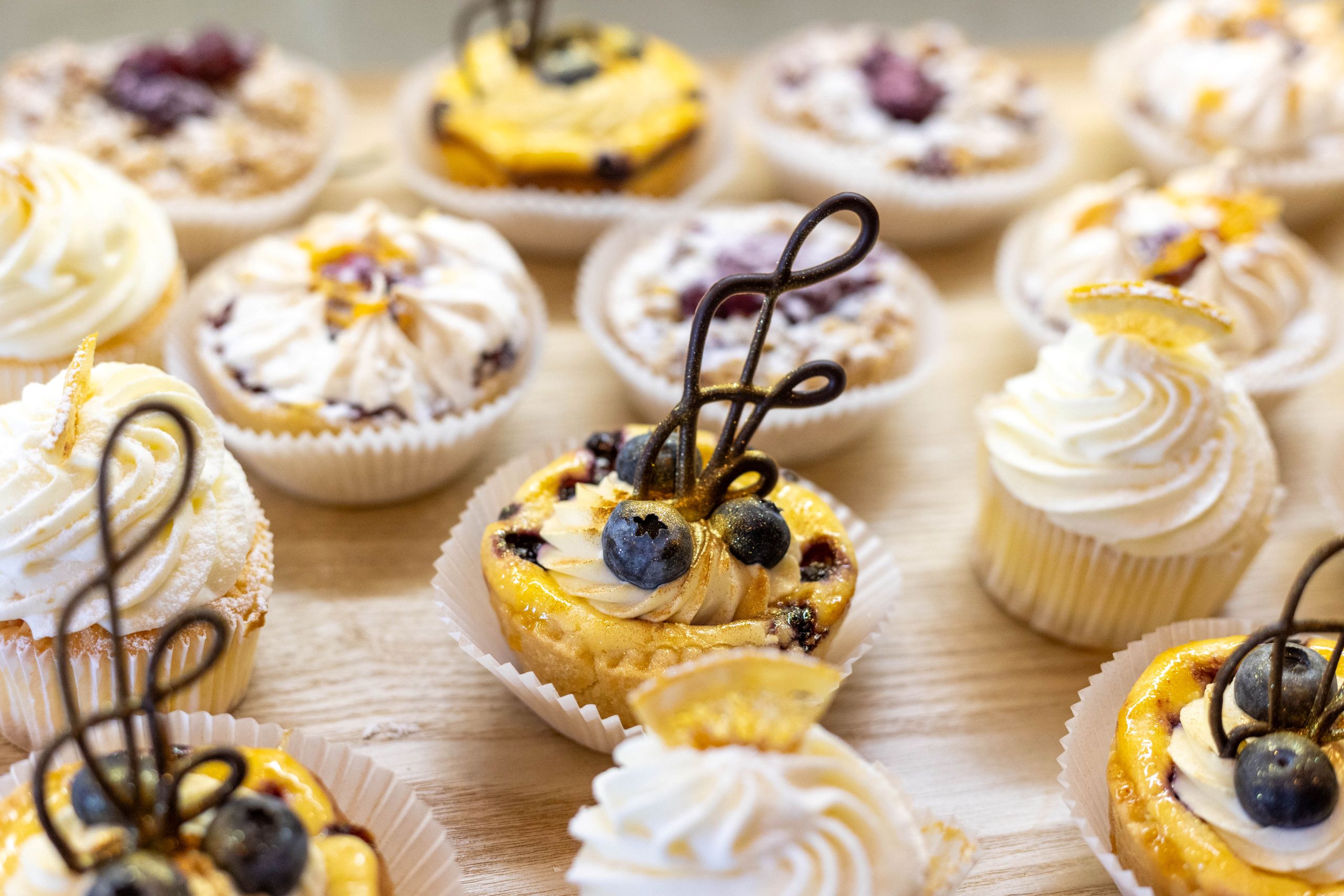 Mehrere Mini-Tartelettes teilweise mit Sahnehäubchen und kandierten Zitronenscheiben oder mit Blaubeeren und schokoladenschnörkel verziert.